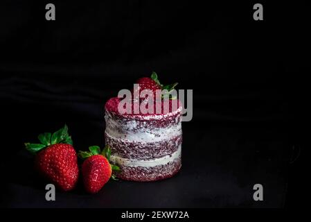 Deliziosa torta di velluto rosso con frutti di fragola su un tavolo nero, primo piano, isolato Foto Stock