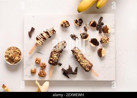 Lecca di banana surgelata o lecci con noci spruzzare per i bambini su bianco. Dolci vegani facili. Vista dall'alto. Foto Stock