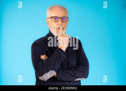 Uomo senior con capelli grigi che indossa un maglione casual in piedi su sfondo blu isolato chiedendo di essere tranquillo con il dito sulle labbra. Silenzio e concep segreto Foto Stock