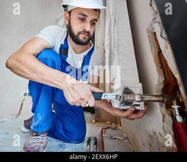 Istantanea orizzontale dei bei raccordi idraulici di avvitamento idraulico con una chiave. Primo piano di un braccio robusto che lavora con un utensile durante i lavori di installazione in un nuovo appartamento. Concetto di costruzione Foto Stock