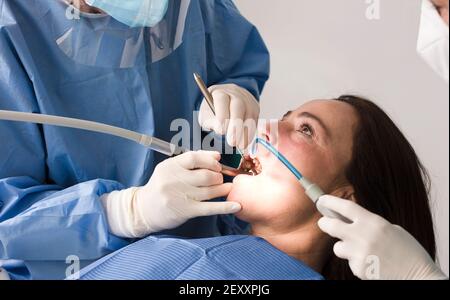 dentista che lavora con dispositivi di protezione individuale, paziente femminile, sulla sedia, sfondo bianco. Durante la pandemia del coronavirus. Foto Stock