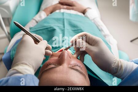 dentista che lavora con dispositivi di protezione individuale, paziente femminile, sulla sedia. Durante la pandemia del coronavirus. Foto Stock