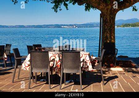 Sedie e tavoli di caffè all'aperto che si affaccia sul Lago di Garda, il più grande lago d'Italia e una popolare località turistica ai margini delle Dolomiti di No Foto Stock