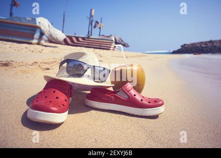 pantofole, cappello, cocco e soffocamento sulla sabbia vicino al mare Foto Stock