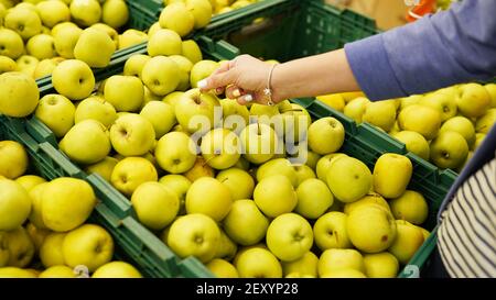 La mano femminile sceglie le mele verdi nel negozio, consumismo e concetto di acquisto. Foto Stock