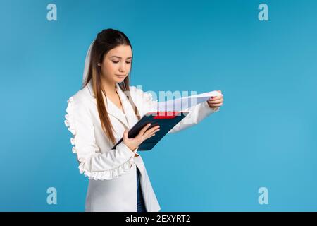 Giovane donna di affari fiduciosa con gli appunti. Ritratto di riuscito imprenditore che tiene gli appunti. Donna che indossa un cappotto bianco e che tiene documenti Foto Stock
