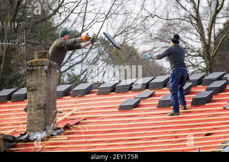 Occupazioni professionali: Due tiler maschili che gettano e impilano le tegole per ri-tegole un tetto, Inghilterra, Regno Unito Foto Stock