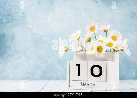 Calendario cubo bianco per marzo decorato con fiori margherita sopra sfondo blu con spazio per la copia Foto Stock