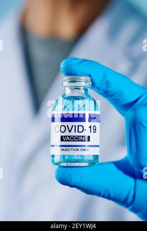 un operatore sanitario o di laboratorio, indossando guanti chirurgici blu, tiene in mano una bottiglia vaccinale simulata di covid-19 Foto Stock