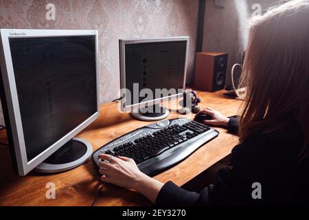 una ragazza sta digitando su una tastiera, lavorando su un personal computer da casa, un uomo è seduto di fronte a due monitor Foto Stock