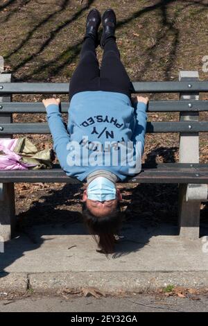 Una donna asiatica americana, probabilmente cinese, fa un tratto molto inusuale capovolto su una panchina in un parco a Queens, New York City Foto Stock