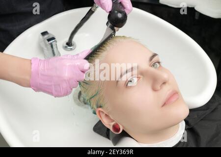 Professionale parrucchiere in guanto protettivo pettinando i capelli verdi del cliente, mentre lavando i capelli nella doccia in speciale salone di bellezza lavabo. Foto Stock