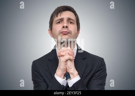 Divertente giovane uomo d'affari sta pregando o chiedendo aiuto. Foto Stock