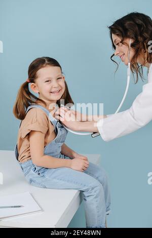 Sorridente medico amichevole che esamina la bambina felice con uno stetoscopio. Ha due ponytail, sorridendo radiosamente alla macchina fotografica. Vista laterale. Finito Foto Stock