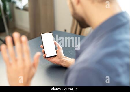 Focus sullo schermo del telefono, vista posteriore di un dipendente maschio che parla, parlare in videochiamata, agitando la mano, conferenza di gruppo con webcam, in ufficio, spazio di copia, mock-up, spazio vuoto Foto Stock