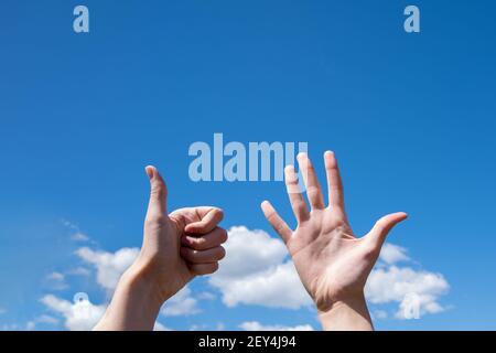 Gesto closeup di una mano di una donna che mostra una palma aperta e pollice su isolato su uno sfondo blu cielo con nuvole, segno lingua simbolo numero sei Foto Stock