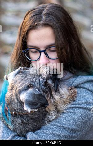 Ritratto di una bruna ragazza in occhiali tiene un cucciolo, cane, schnauzer in miniatura tra le sue braccia. Il concetto preferito degli animali domestici. Foto Stock