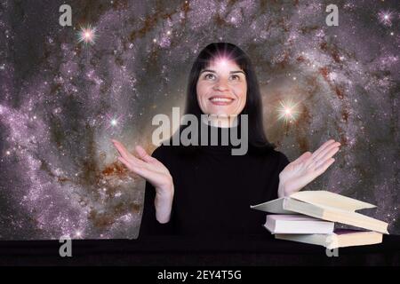 Una ragazza positiva in vestiti neri si siede ad un tavolo con i libri sullo sfondo del cielo stellato. Sulla fronte della ragazza è presente un luminoso simbolo stellare Foto Stock