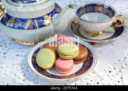 Biscotti macaron con teiera e coppa in ceramica, tovaglia ricamata bianca Foto Stock