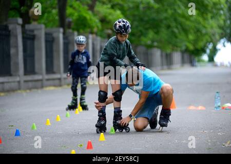 Rollerblading. Trainer corregge i movimenti delle gambe del ragazzo insegnando slalom artistico. 25 giugno 2019. Kiev, Ucraina Foto Stock