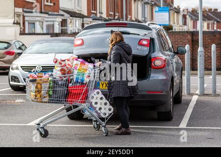 Una donna che carica acquisti o generi alimentari da un carrello o carrello di shopping nella sua automobile Foto Stock