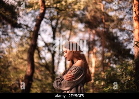 Vista laterale della ragazza adolescente pensierosa in piedi nella foresta durante estate Foto Stock