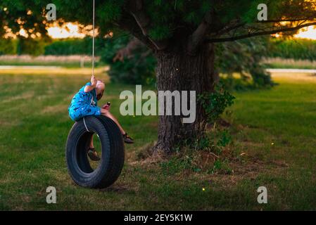 ragazzo in pigiama su swing pneumatico con flash luce che raccoglie mosche di fuoco Foto Stock