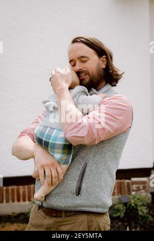 Dolce padre abbracciare figlio neonato in colori pastello fuori in primavera Foto Stock