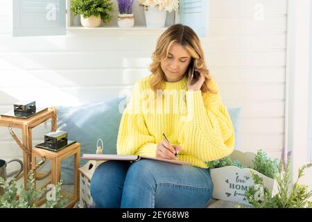 la giovane donna pensiva parla sul telefono scrive nel concetto del notebook di lavorare online all'aperto giallo Foto Stock