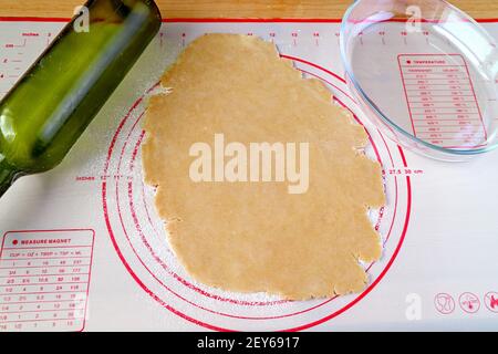 Impastare dopo averla arrotolata su una teglia da forno con cottura in vetro piatto e bottiglia di vino utilizzati come perno di rotolamento Foto Stock