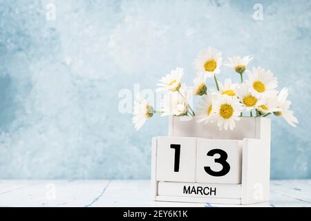 Calendario cubo bianco per marzo decorato con fiori margherita sopra sfondo blu con spazio per la copia Foto Stock