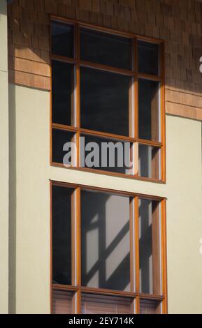 finestra esterna in vetro per la casa con cornici in legno su una casa in cemento il cedro della parete scuote il legno che brilla sulla parete la luce del sole che splende attraverso ombre di fusione delle finestre Foto Stock