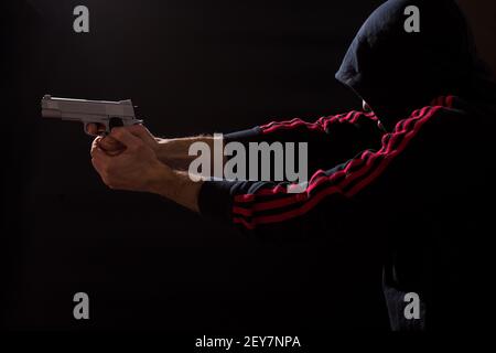 Uomo in sport indossare puntando con pistola su sfondo nero. Foto Stock