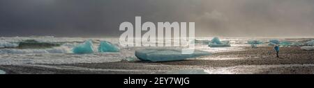 La figurina di un piccolo uomo scatta una foto di le onde infurianti durante una tempesta invernale e l'incredibile la bellezza dei galleggianti di ghiaccio ultramarini sulle rive di Foto Stock