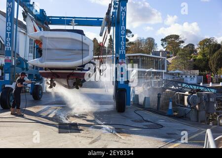 Lo scafo di una barca viene pulito sul porto utilizzando uno spray ad alta pressione a getto d'acqua presso Mylor Yatch Marina vicino Falmouth in Cornovaglia prima dello stoccaggio. Foto Stock