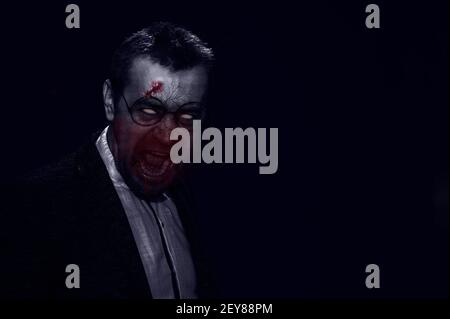 Scena horror di un uomo dal volto sanguinoso. Zombie in giacca e bicchieri. Immagine a toni. Concetto di orrore Foto Stock