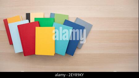 Vista dall'alto di un mucchio di libri colorati e luminosi su una scrivania in legno chiaro con spazio per il testo. Foto Stock