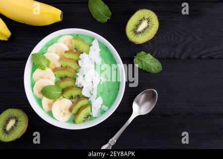 Ciotola per frullati con banana, kiwi e patatine di cocco sullo sfondo di legno nero.Vista dall'alto.spazio copia. Foto Stock