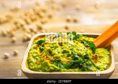 Hummus di ceci fatto in casa con erbe in ciotola quadrata di legno di bambù, bastone di carote Foto Stock