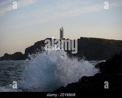 L'acqua dell'onda di mare che colpisce la rottura sulla riva rocciosa alla costa della scogliera dell'oceano atlantico Punta Frouxeira Torre del faro a Meiras Valdovino la Coruna, Foto Stock