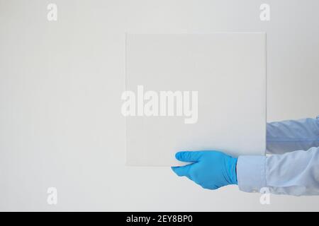 Addetto alla consegna che tiene scatole di cartone in guanti medici su sfondo bianco. Il tempo di spedizione coronavirus. Foto Stock