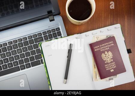 KATOWICE, POLONIA - 12 febbraio 2021: Scrivania con vista dall'alto con computer portatile, notebook, passaporto, banconota e caffè. Foto Stock