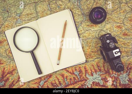 KATOWICE, POLONIA - 12 febbraio 2021: Quaderno con lente di ingrandimento e matita sdraiato su una vecchia mappa accanto a una fotocamera d'epoca Foto Stock