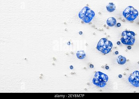 Perline di vetro blu e bianco con perline in argento, su superficie di legno verniciata di bianco, vista dall'alto verso il basso Foto Stock