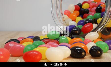 Chicchi di gelatina colorati che fuoriescono da un vaso di vetro sul tavolo. Spazio vuoto nell'angolo superiore per il messaggio Foto Stock