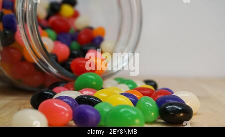 Chicchi di gelatina colorati che fuoriescono da un vaso di vetro sul tavolo. Spazio vuoto nell'angolo superiore per il messaggio Foto Stock