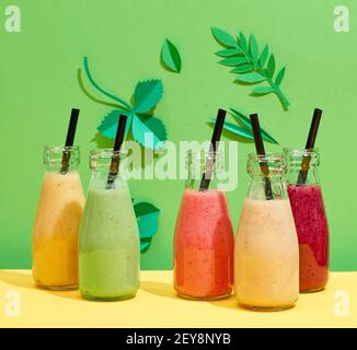 bottiglie di vari smoothies colorati di banana e di bacche su verde sfondo foglio di carta Foto Stock