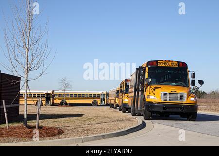 Augusta, GA USA - 03 05 21: Fila di autobus della scuola gialli nuovi e vecchi parcheggiati in fila dietro un angolo Foto Stock