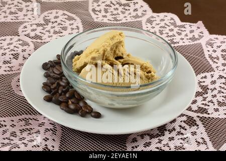 Caffè gelato in recipiente di vetro e caffè in grani piatto bianco su runner da tavolo in pizzo con cuore rosa su marrone tovaglia Foto Stock