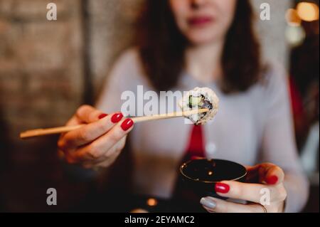 Un primo piano della mano di una donna che tiene un appetitoso Salmone tradizionale giapponese di sushi in bastoncini e immersione del rotolo in salsa di soia Foto Stock